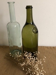2 bouteilles en verre. L'une est vert foncé. Une branche de fleurs blanches est posé devant